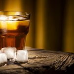 A glass of alcoholic beverage on a wooden table. Whiskey cocktail with ice